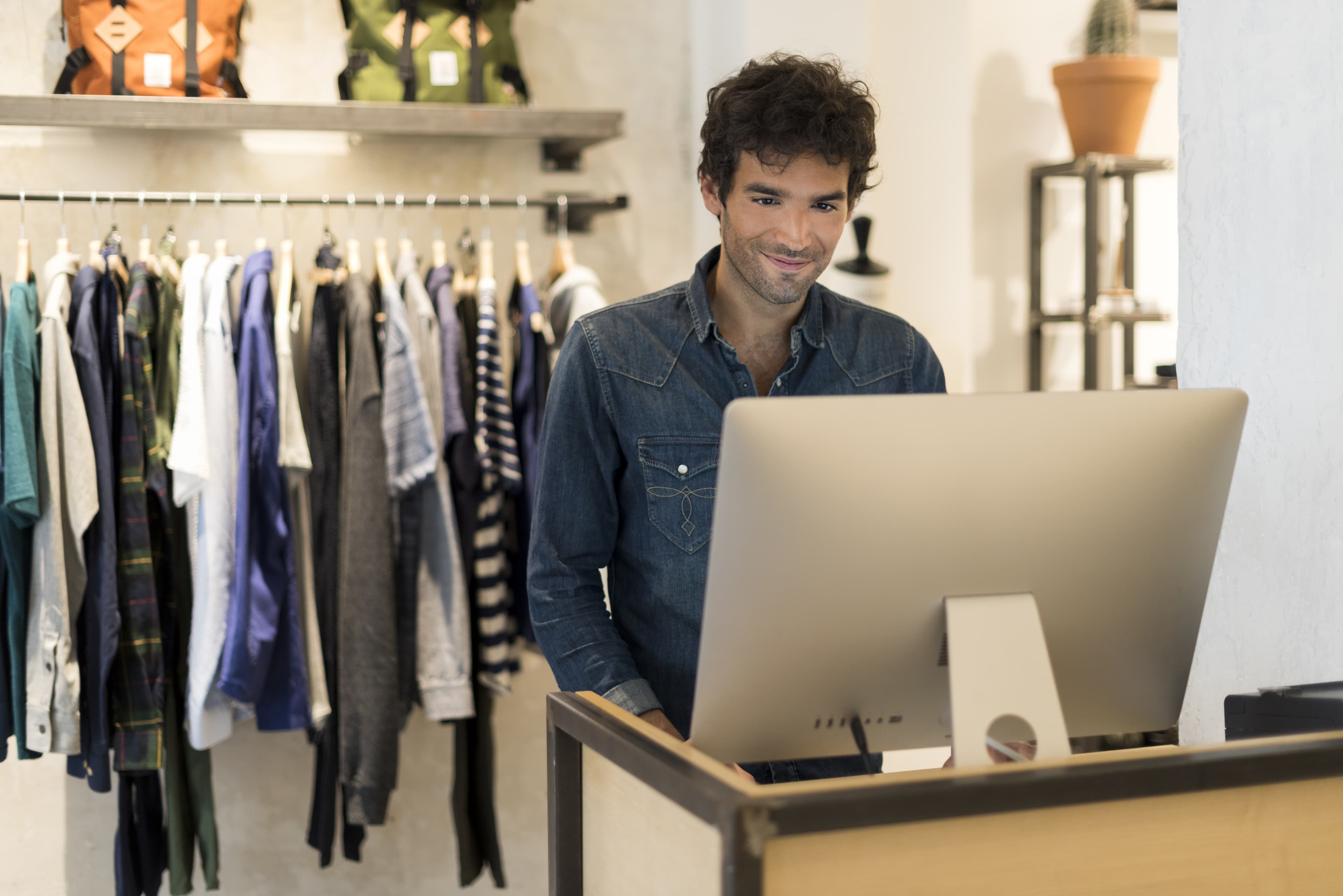 male store associate looking at a desktop computer in a clothing store