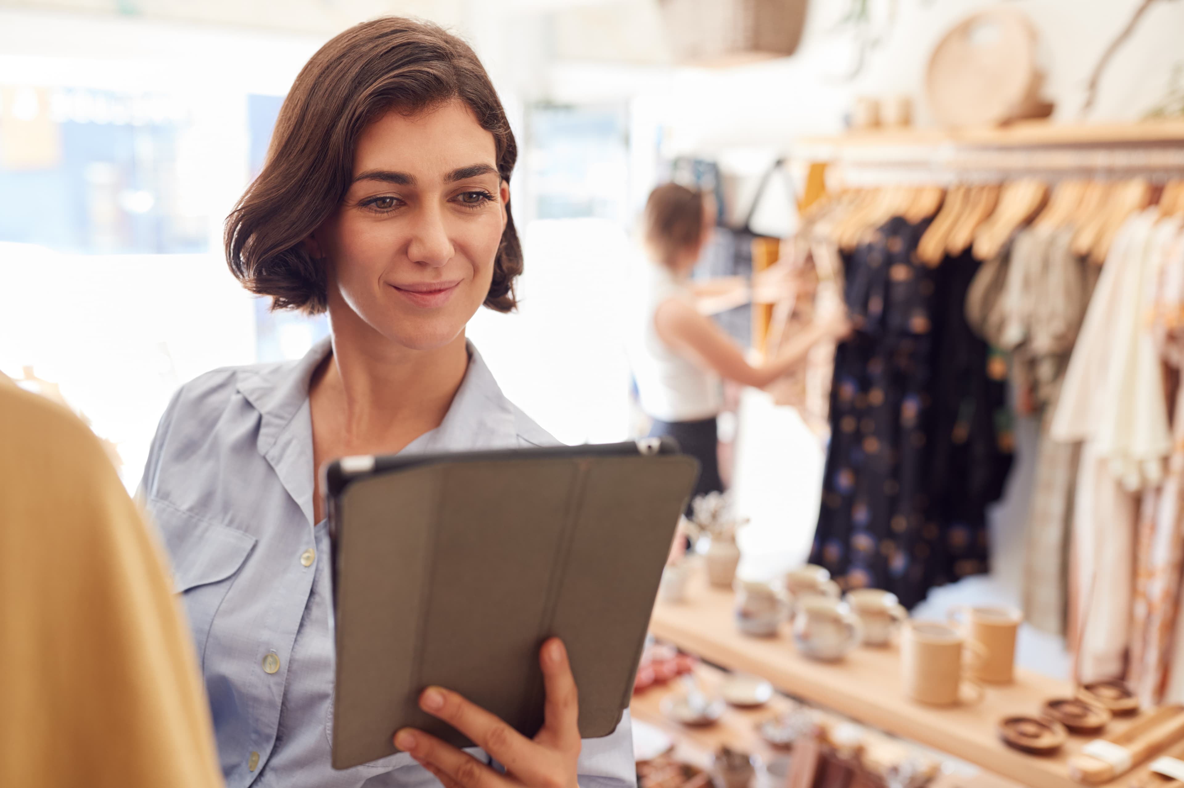 Female Owner Of Fashion Store Using Digital Tablet To Check Stock On Rails In Clothing Store