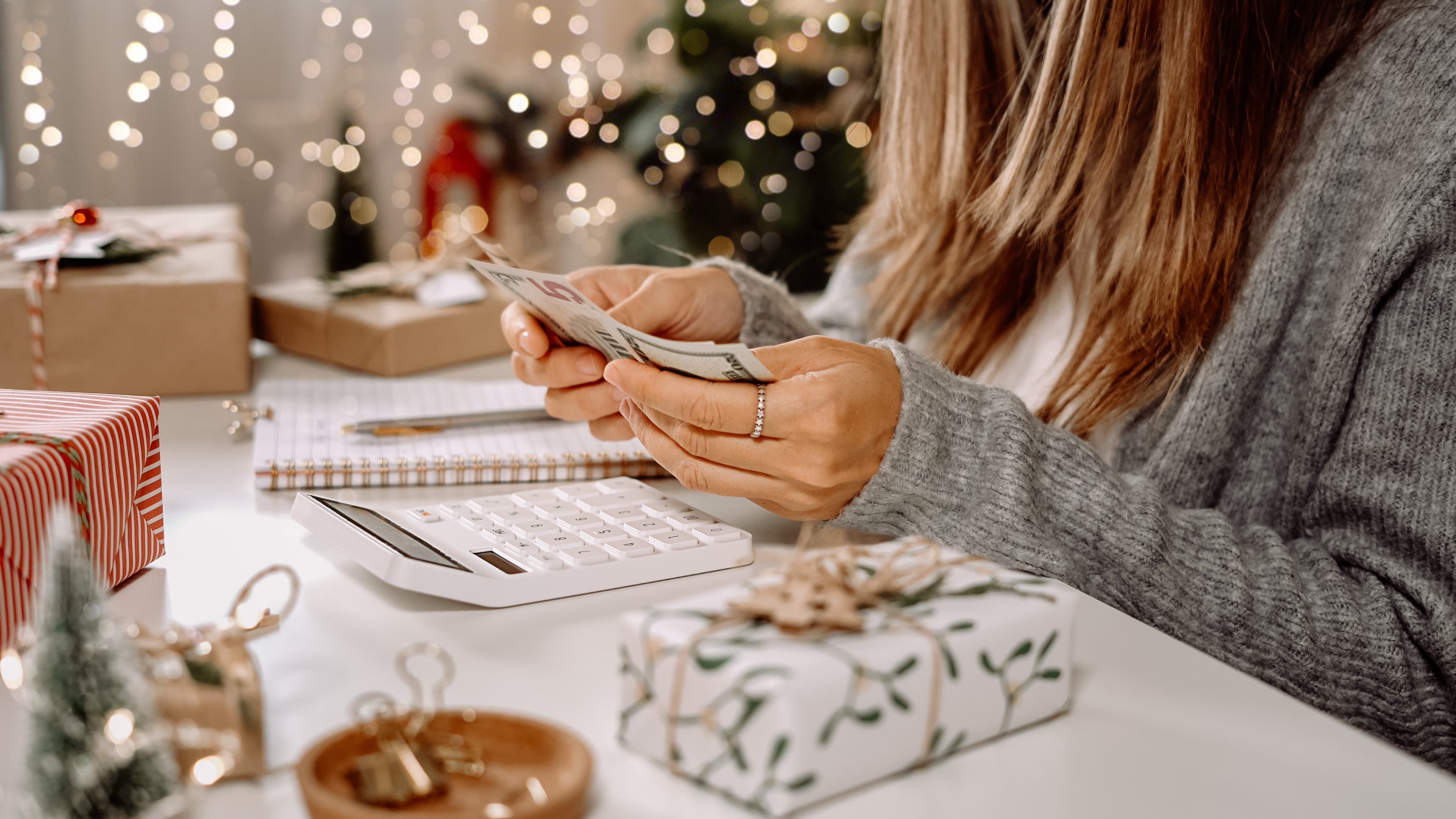 woman sitting at desk with calculator, counting money in front of festive background